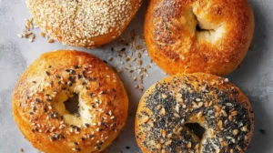 Four cottage cheese bagels with different seed toppings on gray background